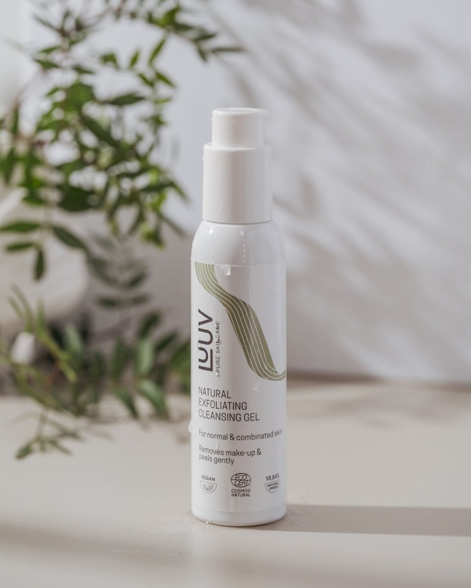 Vit flaska med pump för Naturlig Exfolierande Rengöringsgel med grön våglinje-design mot ljus bakgrund med växt