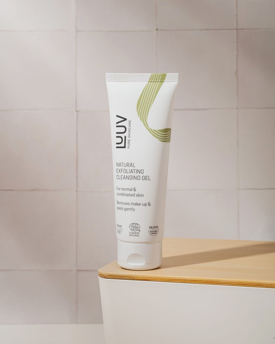 Vit tub med naturlig exfolierande rengöringsgel, gröna designelement, stående på träyta mot kaklat badrum