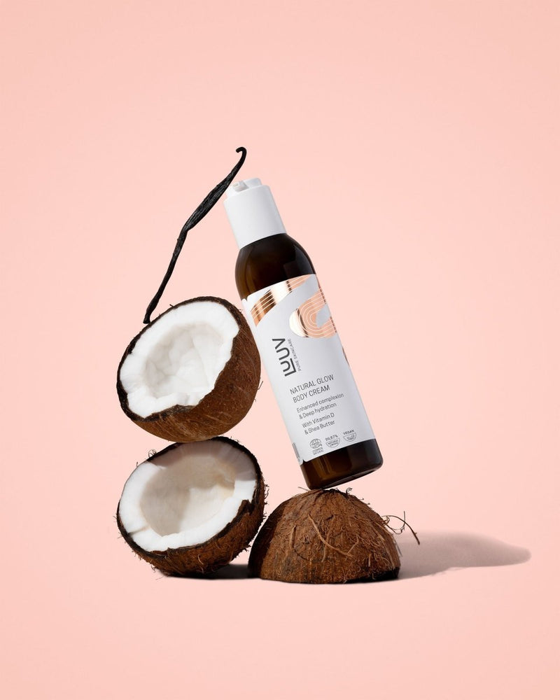 Natural Glow kroppskräm i brun glasflaska mellan halverad kokosnöt och vaniljstång