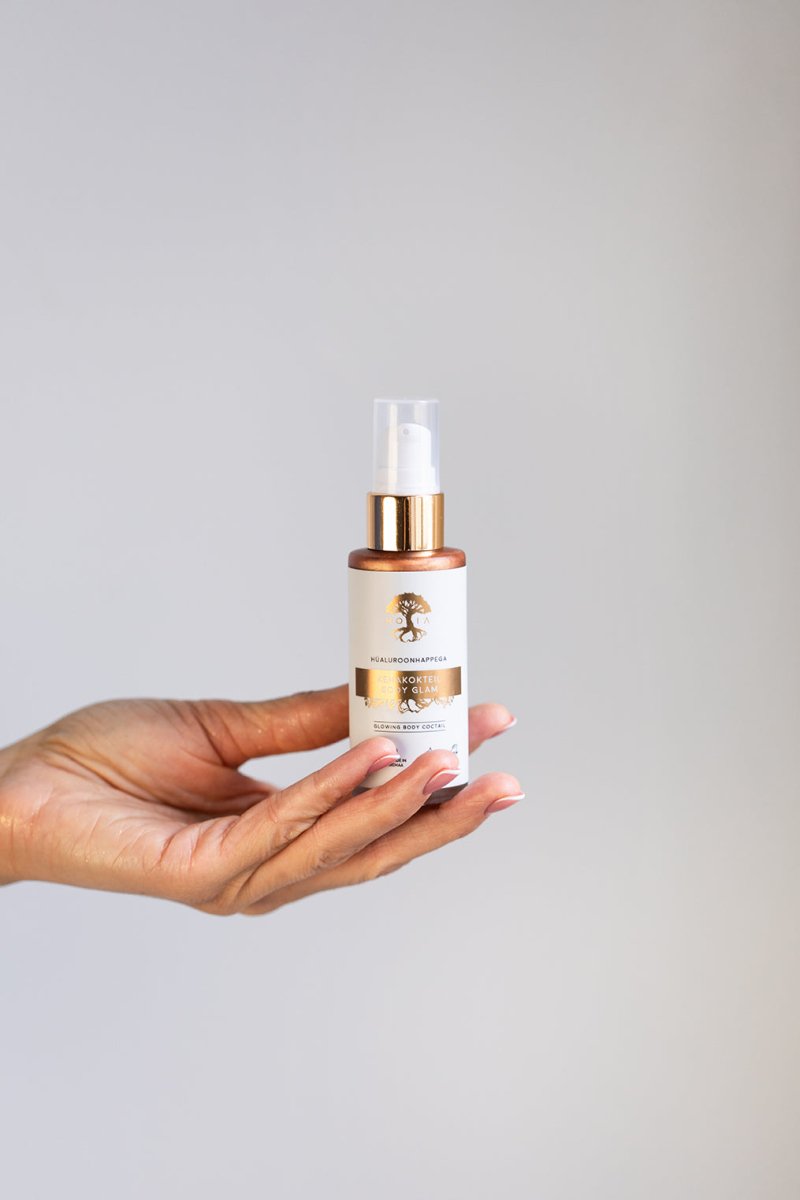 Hand som håller en liten sprayflaска med Kroppslotion Body Glam 50ml med gulddetaljer mot neutral bakgrund