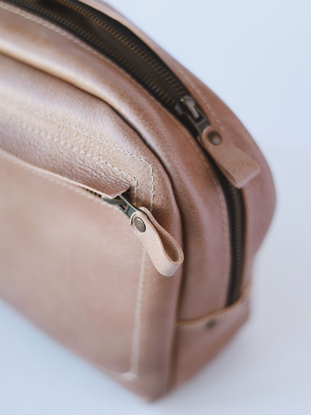 Handgjord necessär i beige läder med dragkedja och mjuk textur, fotograferad från sidan mot vit bakgrund