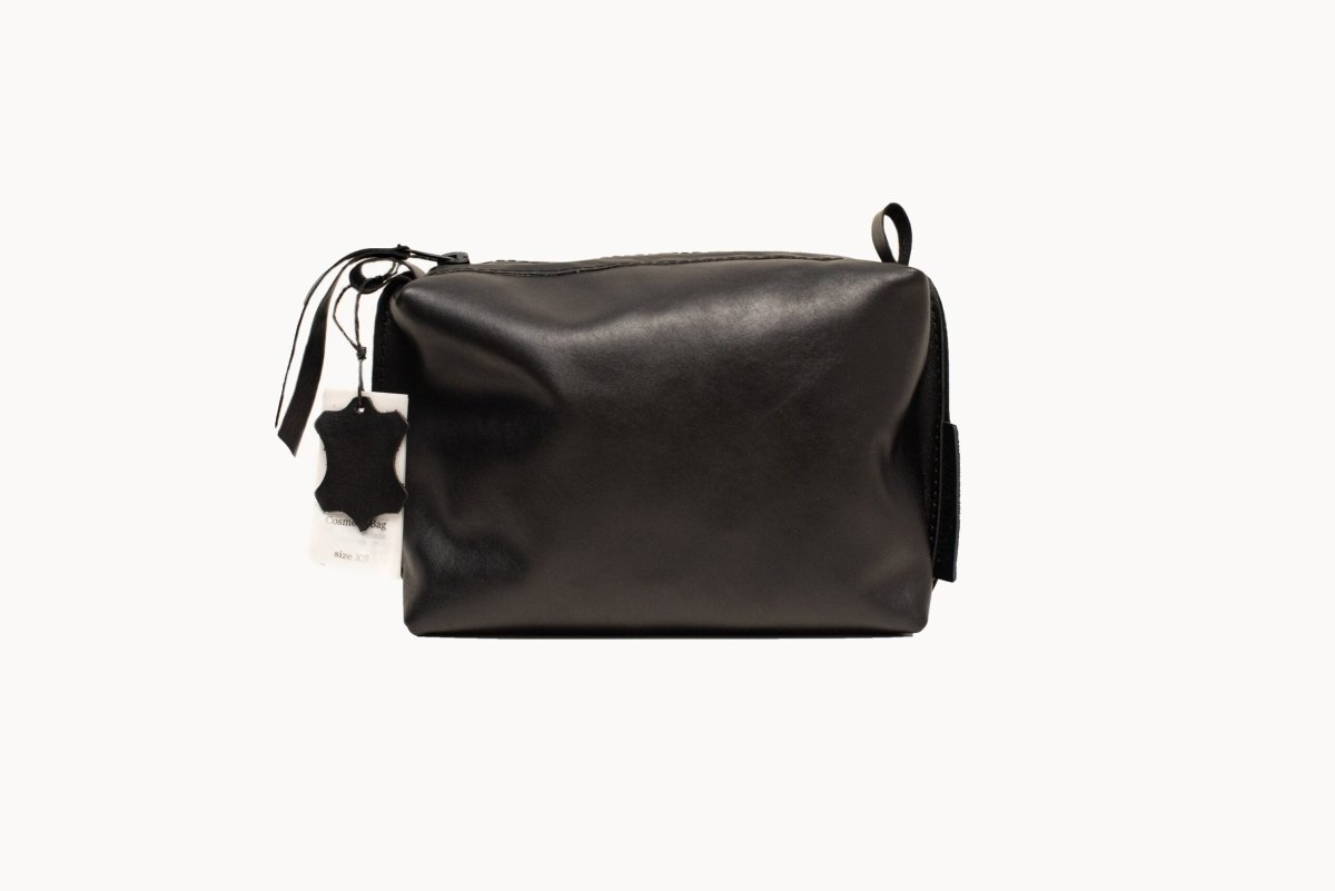 Necessär i Läder, Svart - Medium: elegant svart läderväska med dragkedja, handtag och prislapp mot vit bakgrund