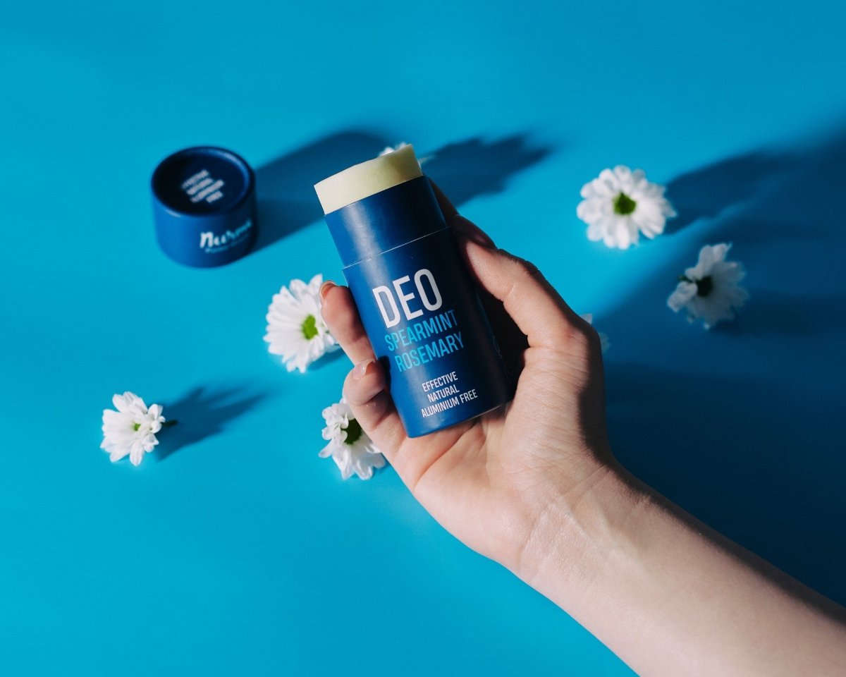 Nurme Naturlig Deodorant Grönmynta & Rosmarin i blå förpackning med guldlock hålls i hand mot turkos bakgrund