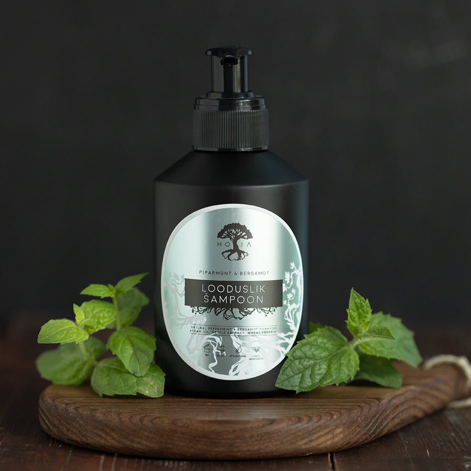 HOIA ekologiskt schampo utan sulfater med pepparmint och bergamot i svart pumpflaska, omgiven av färska mintblad