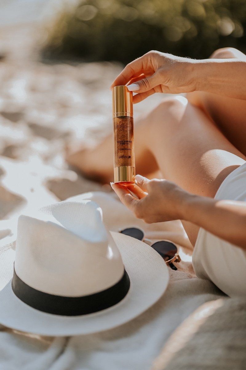 Glow Oil 50ml i elegant glasflaska med guldlock hålls i händerna, oljans gyllene färg syns genom glaset