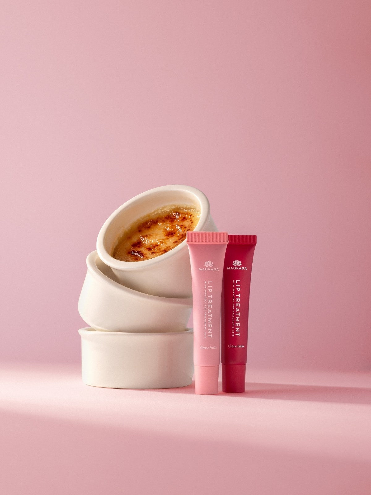 Två tuber tonad läppbalsam med hyaluronsyra i rosa och cerise mot rosa bakgrund