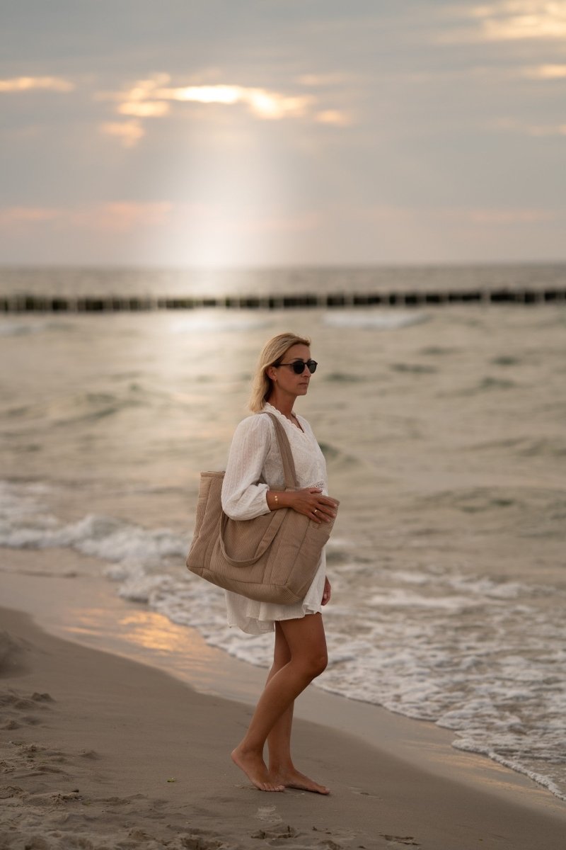 Kvinna bär handgjord weekenderbag i latte-sammet från Moi Mili på stranden vid solnedgång