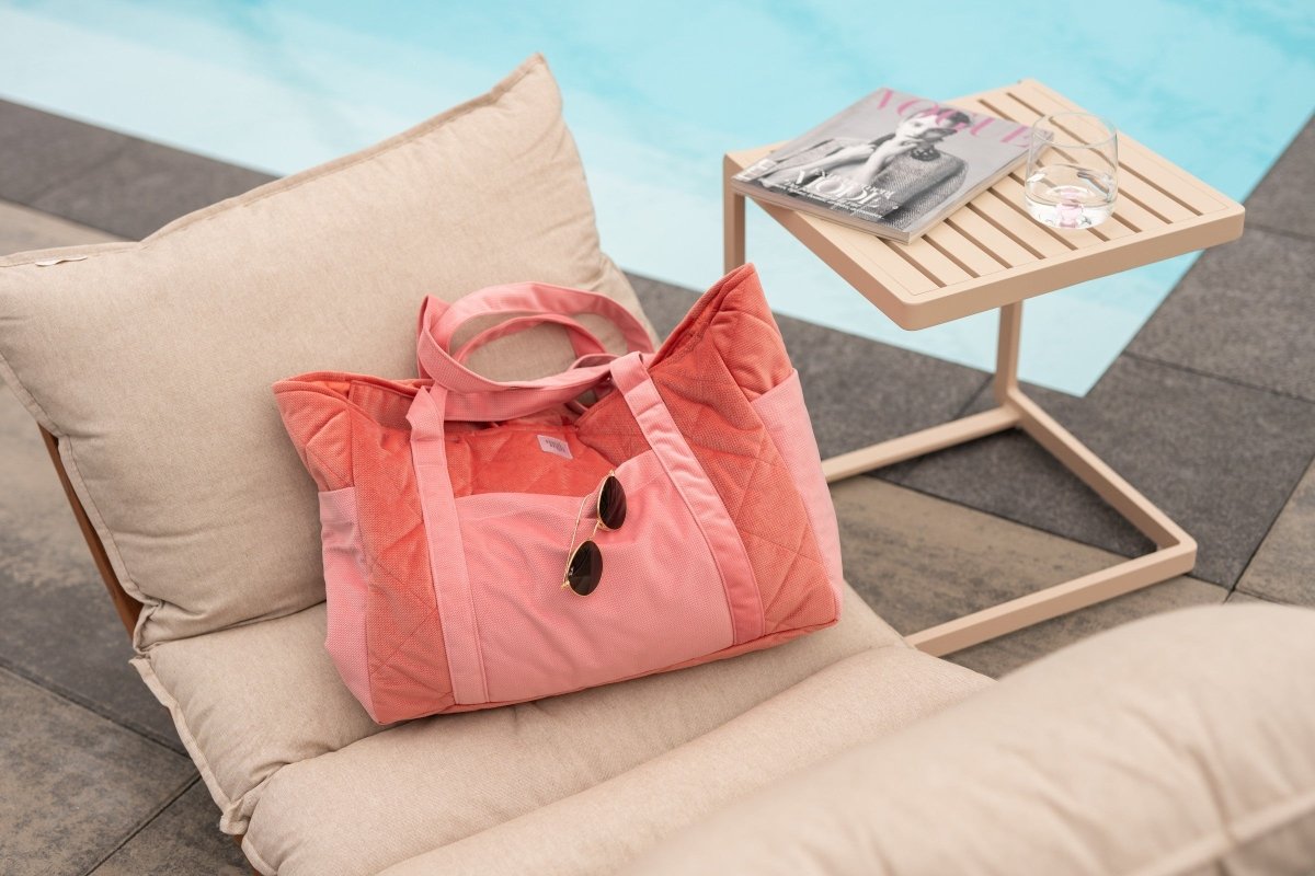 Handgjord weekenderbag i rosa sammet vid poolen, med solglasögon och magasin på sidobord